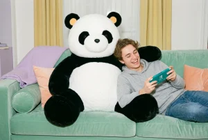 Peluche panda géante assise sur un canapé vert à côté d’un joueur